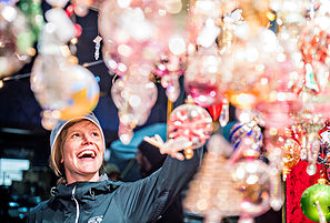 A woman reaching for a holiday glass ball with lots of twinkly lights during a Winter German market called Christkindl, Denver, Colorado.